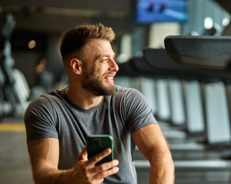 Portrait of a young man using a phone ant exting taking a break exercising in a gym, running using  thereadmill machine equipment, healthy lifestyle and cardio exercise at fitness club concepts