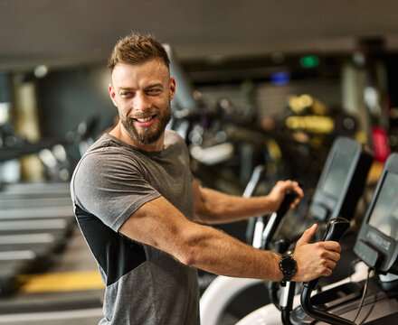 Portrait of a young man exercising on an elliptical trainer in a gym, running using  thereadmill machine equipment, healthy lifestyle and cardio exercise at fitness club concepts - Powered by Adobe