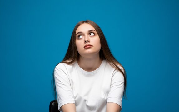 Woman rolling eyes upward in boredom on blue background, unimpressed facial expression portrait