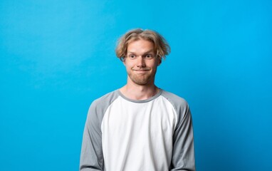 Calm young man standing against bright blue background with relaxed neutral facial expression