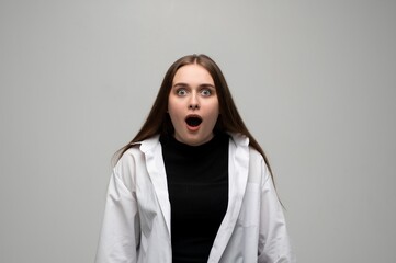 Young woman looking shocked with wide eyes and open mouth in studio portrait on gray background