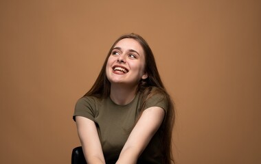 Smiling young woman looking up with joyful expression on brown background, positive human emotion portrait