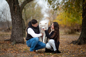 A young family - a guy, a girl and a cute fluffy Samoyed - are walking by the river