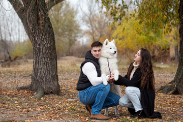 A young family - a guy, a girl and a cute fluffy Samoyed - are walking by the river