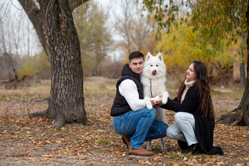 A young family - a guy, a girl and a cute fluffy Samoyed - are walking by the river