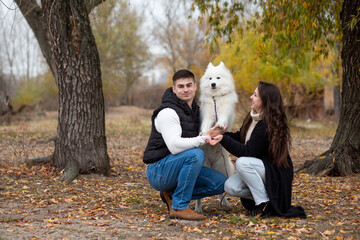 A young family - a guy, a girl and a cute fluffy Samoyed - are walking by the river