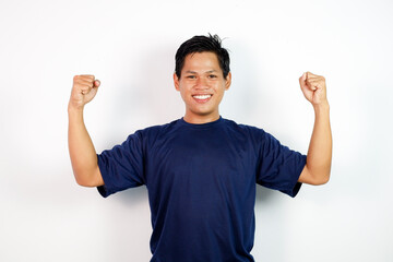 Confident Young Asian Man Raising Arms in Victory Pose Wearing Navy T-Shirt Against White Background Studio
