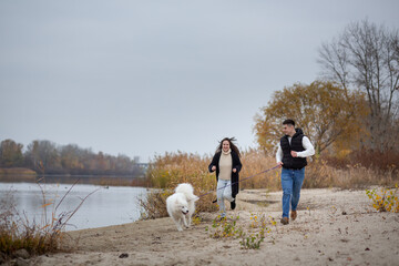 A young happy family runs along the banks of the Dnieper with their cute, furry pet, a Samoyed