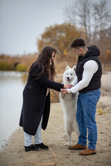 A family - a young man and a girl holding a cute fluffy Samoyed on the banks of the Dnieper River