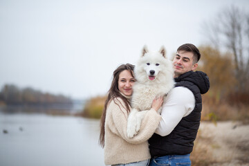 A family - a young man and a girl holding a cute fluffy Samoyed on the banks of the Dnieper River