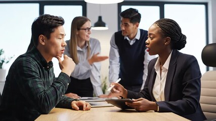 Diverse business team collaborating around a table, discussing data on a digital tablet during a modern office meeting - Powered by Adobe
