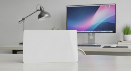Mockup of a closed white laptop on a clean desk in front of a computer monitor and a modern desk lamp in a bright office setting