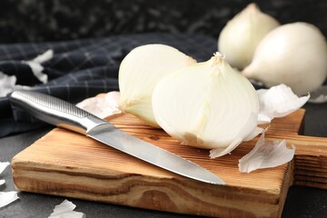 Cut onion bulbs with peels and knife on black table, closeup