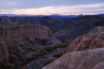 Charyn Canyon scenic canyon in Kazakhstan at sunset or sunrise. Light rocks, dark riverbed with autumn vegetation and mountains on the horizon create an atmosphere of tranquility.