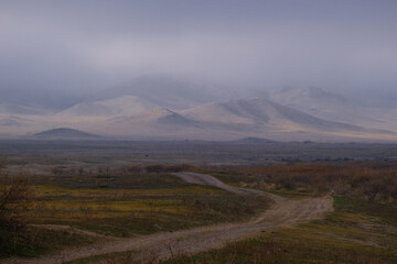 The country road goes off into the distance, towards the hills hidden by the fog. The sky is gray and overcast, the landscape looks dull and thoughtful. Nature in autumn colors