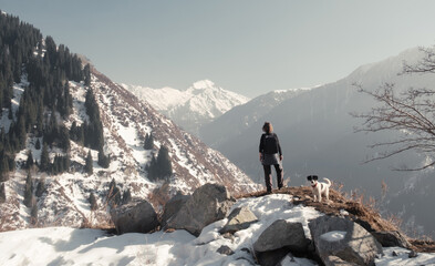 A woman with a dog on a snowy mountainside. They look at the majestic mountains. There is snow and...
