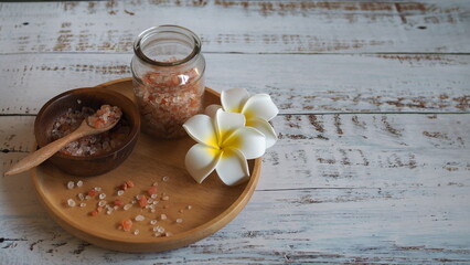 Himalayan salt in a jar, along with salt in a bowl and frangipani flowers.