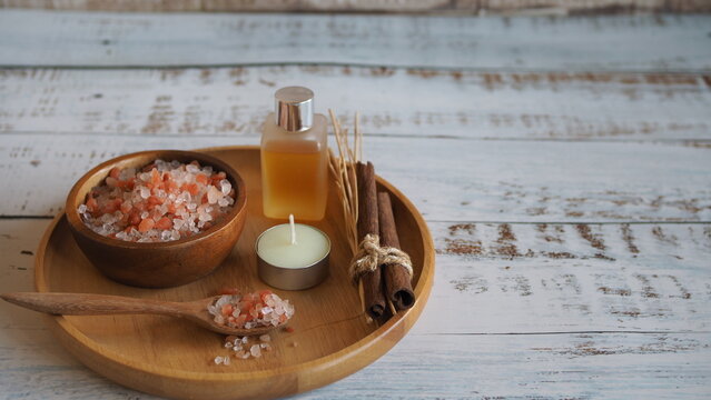 Spa still life with pink bath salt in wooden bowl, essential oil bottle, cinnamon sticks and aroma reeds on rustic wooden table, creating a natural wellness, relaxation and self care concept.