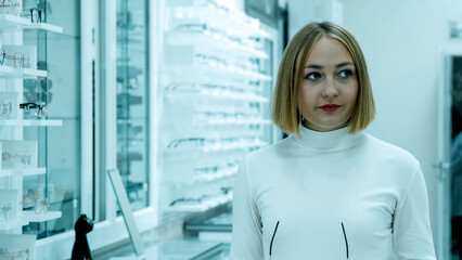 Woman in glasses stands in an optical store, looking at the camera