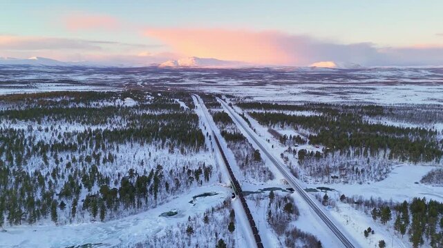Freight train with iron ore, aerial view, Sunset over arctic mountain landscape in Lapland, Sweden, road and railroad between Kiruna and Narvik