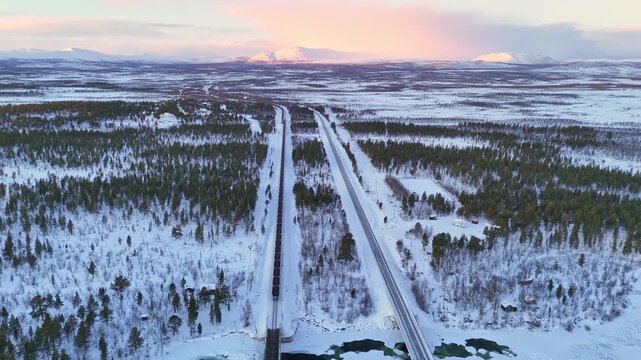 Freight train with iron ore, aerial view, Sunset over arctic mountain landscape in Lapland, Sweden, road and railroad between Kiruna and Narvik