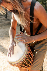 Bearded man playing djembe drum outdoors during tribal music performance at sunset