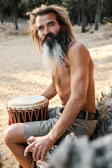 Bearded man sitting outdoors with traditional drum in natural warm sunlight setting