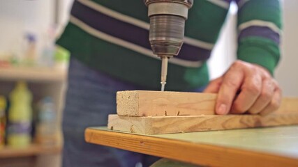 Close-up of worker’s hands removing a screw from wooden board with a cordless drill