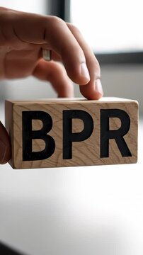 On a clean white surface, a hand gently sets down a wooden block marked with the initials BPR, representing the concept of Business Process Reengineering