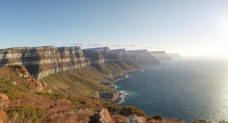 Expansive coastal landscape featuring layered cliffs meeting the sea under a bright sky