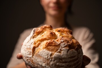 Fresh rustic artisan bread loaf held forward by baker in warm soft light showcasing crisp crust and flour texture