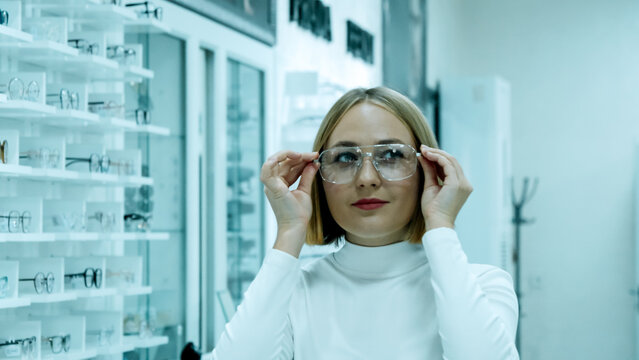 Young woman in glasses looks at the screen of a modern laptop at an office desk