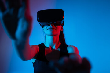 Woman extending arms forward toward virtual interface while wearing VR headset in neon sci-fi lighting