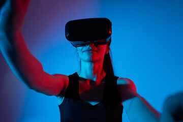 Woman raising arms while wearing VR headset and interacting with virtual elements in neon environment