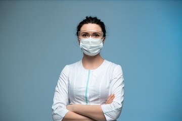 Female doctor in medical mask and protective glasses posing confidently in uniform