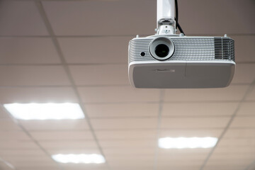 White multimedia video projector mounted on a suspended ceiling in a modern office conference room. Business presentation technology equipment. Photo