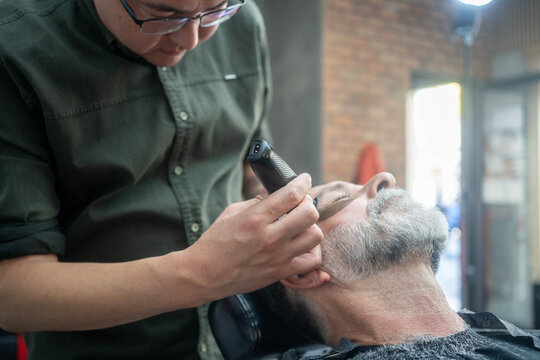 Asian barber grooming mature man’s beard in a professional barbershop
