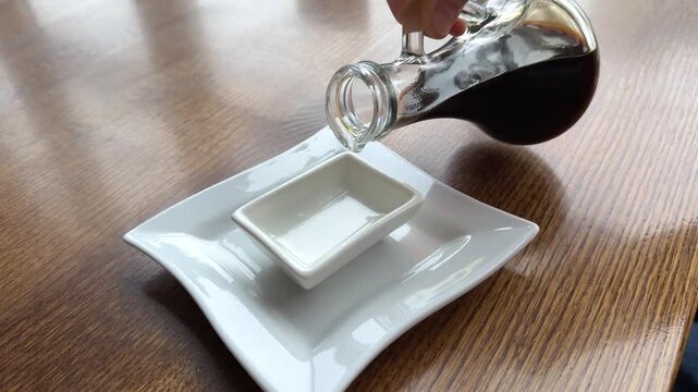 Dark brown soy sauce pouring down into the glass bowl