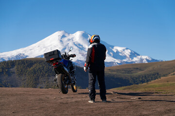 Mountain motorcycle tourism. A biker with a motorcycle against a picturesque backdrop of a snow-capped volcano and blue sky. Copy space. © ROMAN DZIUBALO