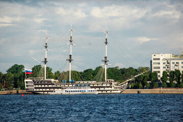 A sailing ship, flying the Russian flag, in St. Petersburg. A modern passenger boat is docked alongside the historic ship. for travel, historical, or nautical-themed content