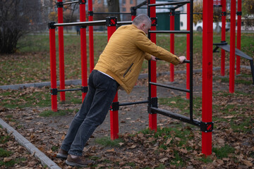 Obraz premium Man exercises on outdoor fitness equipment in urban park during autumn season in the afternoon