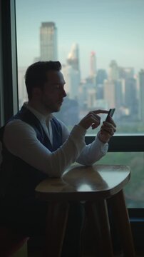 man works remotely, man sitting at table concentrating on his phone with city views passing outside