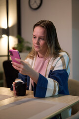 Woman sitting at table looking at smartphone with cup in hand