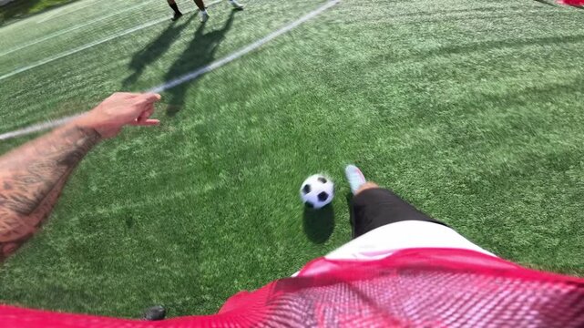 First person perspective of a soccer player kicking a penalty shot. He scores a goal against the goalkeeper on a sunny day in slow motion