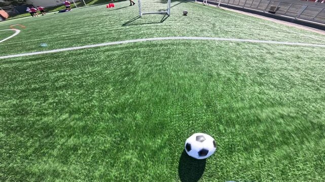 Pov shot of a football player running and dribbling a ball on a green turf field, then kicking it into the net for a goal in slow motion