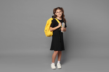Smiling girl in glasses with backpack and notebooks on grey background