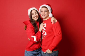 Fototapeta premium Smiling couple in hats hugging on red background. Merry Christmas and Happy New Year