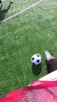 First person view of a soccer player's feet dribbling the ball on a green turf field and then kicking it towards the goal in slow motion