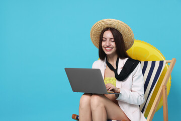 Fototapeta premium Businesswoman with laptop in deck chair and inflatable ring on light blue background, space for text