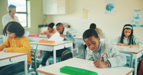 Boy, writing test and learning in classroom at school, assessment and development with scholarship. Child, education and exam paper with problem solving, answer or pupils with evaluation at academy